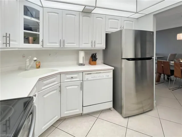 Kitchen with stainless steel appliances, light countertops, white cabinets, and light tile patterned floors
