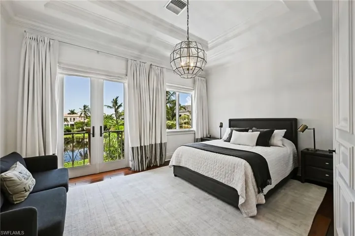Bedroom with a raised ceiling, access to exterior, french doors, crown molding, and a chandelier
