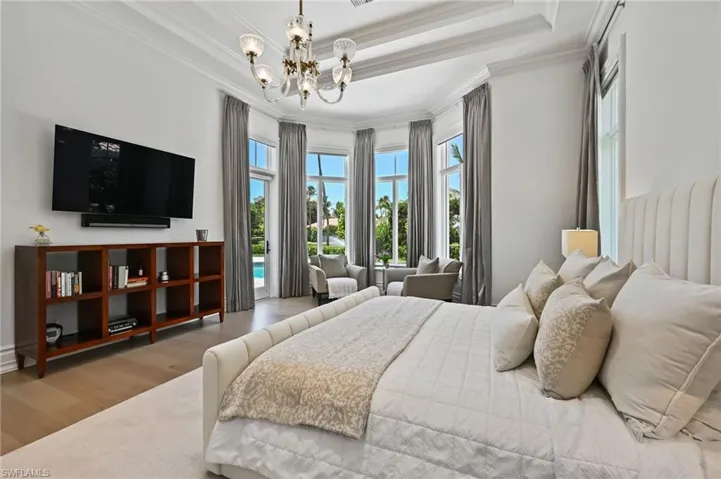 Bedroom with a raised ceiling, wood finished floors, crown molding, a chandelier, and access to outside