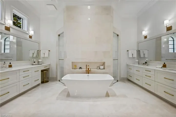 Full bath with ornamental molding, a freestanding bath, two vanities, walk in shower, and a towering ceiling