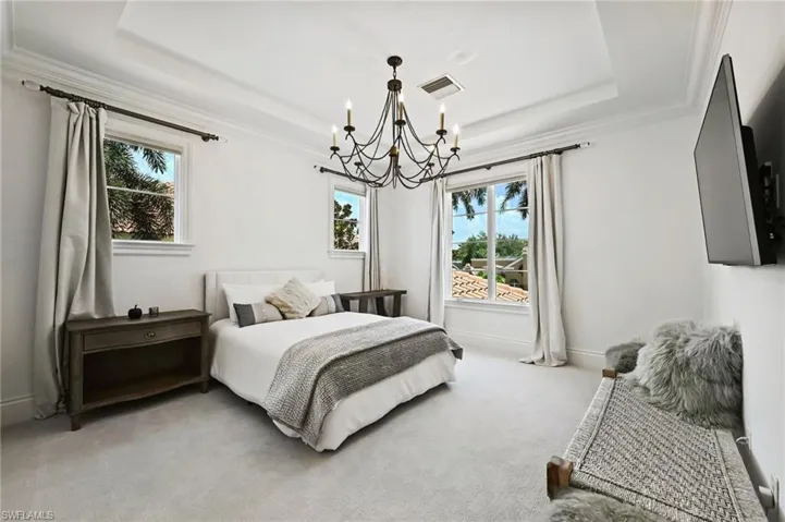 Carpeted bedroom featuring a tray ceiling, ornamental molding, and a chandelier