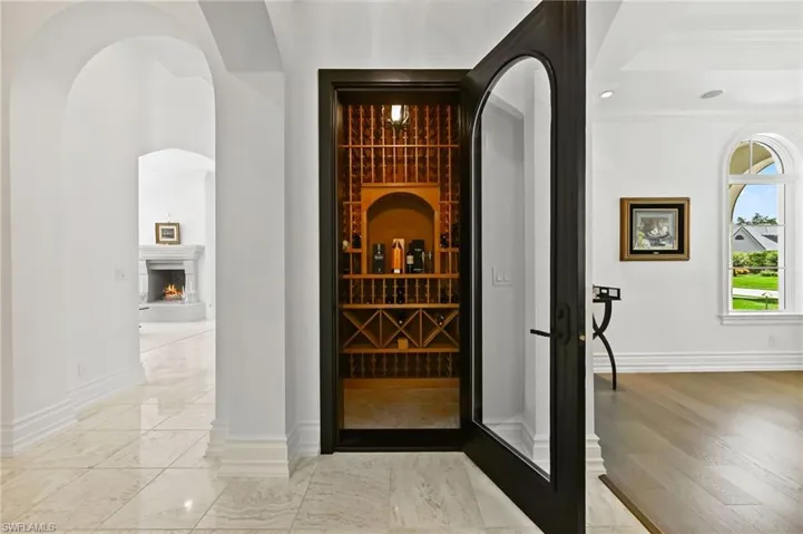 Wine cellar with arched walkways, a warm lit fireplace, and crown molding