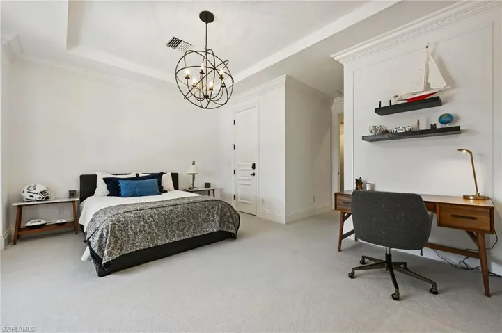 Bedroom with a tray ceiling, light carpet, ornamental molding, an office area, and a chandelier