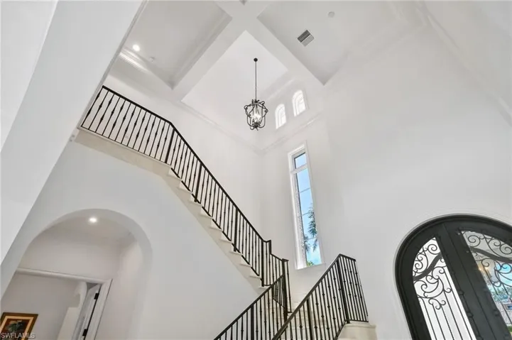 Foyer entrance featuring a towering ceiling, arched walkways, a chandelier, french doors, and stairway