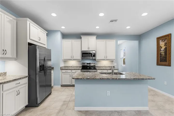 Kitchen featuring appliances with stainless steel finishes, light stone counters, white cabinets, a kitchen island with sink, and recessed lighting