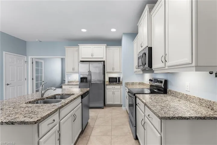 Kitchen featuring appliances with stainless steel finishes, an island with sink, white cabinets, light stone counters, and light tile patterned flooring