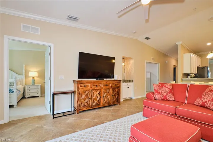 Living room featuring crown molding, light tile patterned floors, ceiling fan, vaulted ceiling, and light carpet