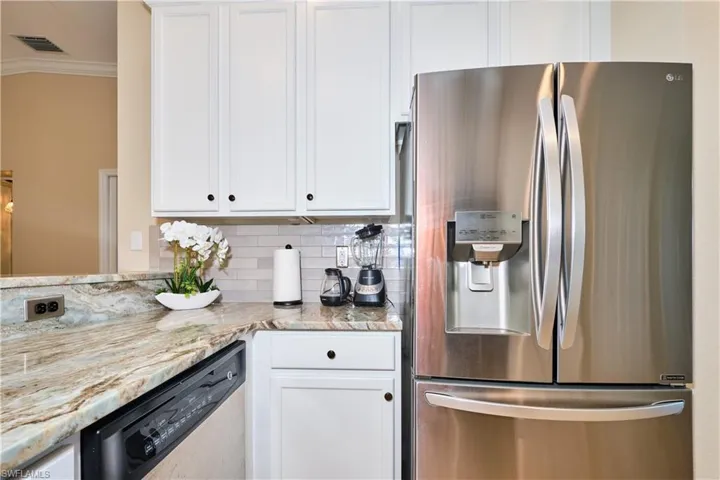 Kitchen featuring stainless steel appliances, crown molding, white cabinets, tasteful backsplash, and light stone counters