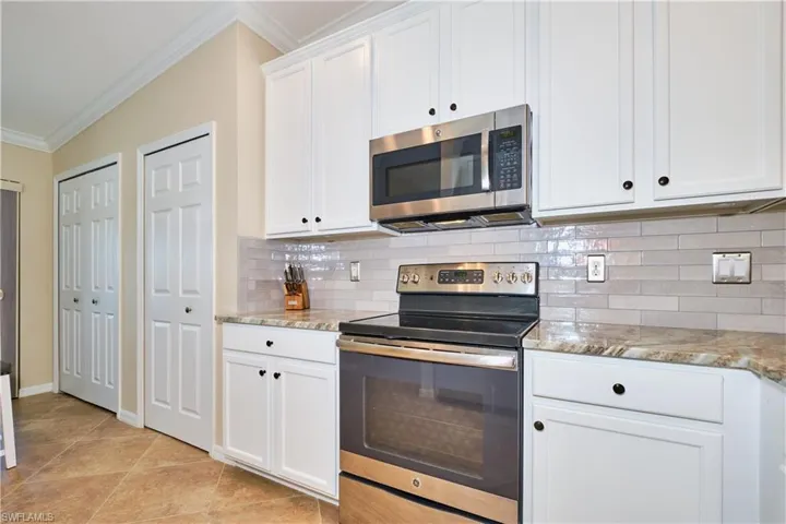 Kitchen with stainless steel appliances, crown molding, tasteful backsplash, white cabinets, and light stone counters