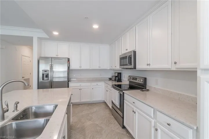 Kitchen featuring white cabinetry, sink, light stone counters, appliances with stainless steel finishes, and light tile patterned floors