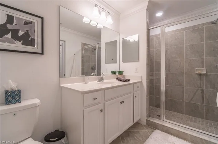 Bathroom with walk in shower, toilet, tile patterned floors, vanity, and ornamental molding