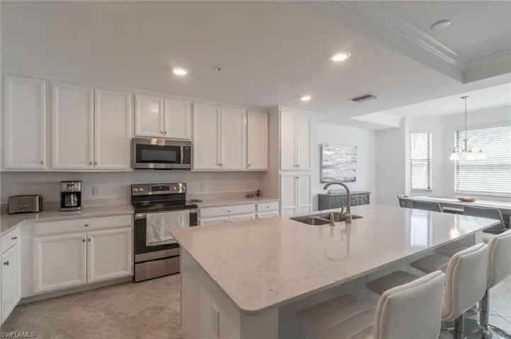 Kitchen featuring sink, appliances with stainless steel finishes, white cabinets, and a center island with sink