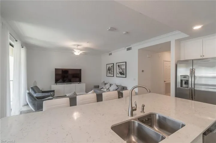 Kitchen with white cabinetry, crown molding, light stone counters, ceiling fan, and sink