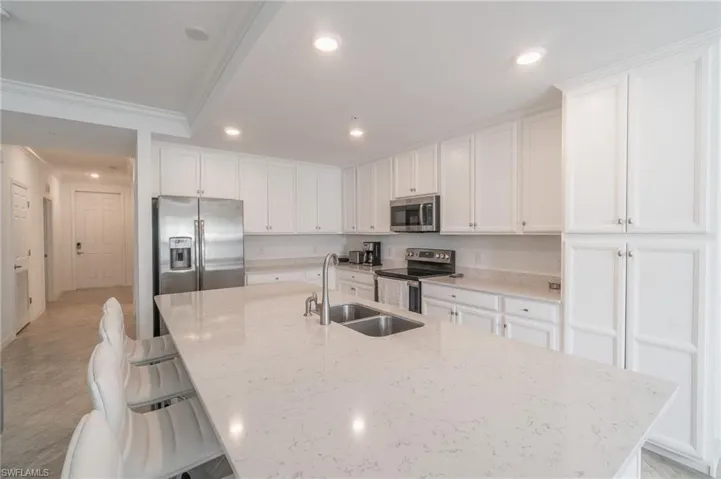 Kitchen featuring sink, a breakfast bar area, light stone countertops, appliances with stainless steel finishes, and a kitchen island with sink