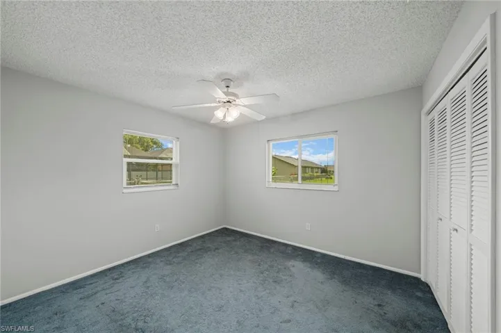 Unfurnished bedroom featuring dark colored carpet, a closet, a textured ceiling, and a ceiling fan