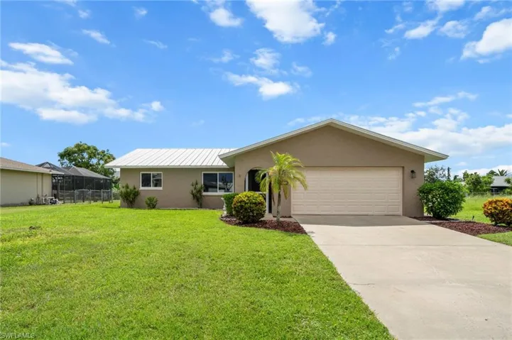 Ranch-style home with stucco siding, driveway, a front yard, a garage, and a metal roof