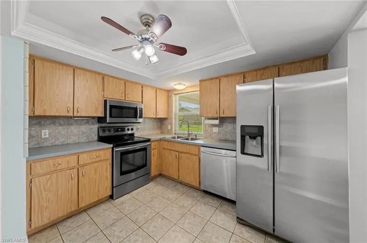 Kitchen featuring a raised ceiling, stainless steel appliances, ceiling fan, ornamental molding, and tasteful backsplash