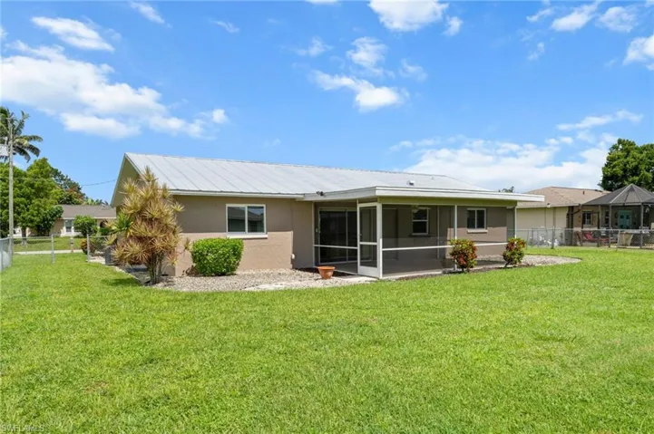 Back of property featuring stucco siding, a sunroom, a fenced backyard, and a metal roof
