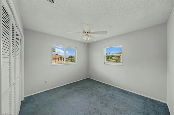 Unfurnished bedroom featuring a textured ceiling, carpet, multiple windows, a closet, and a ceiling fan