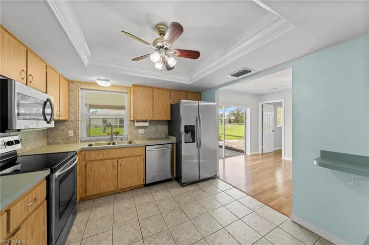 Kitchen with stainless steel appliances, a tray ceiling, light tile patterned flooring, ceiling fan, and crown molding