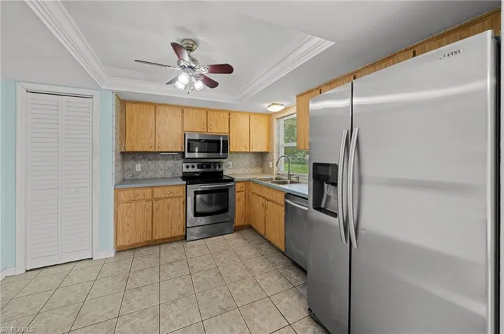 Kitchen with stainless steel appliances, a raised ceiling, crown molding, light tile patterned flooring, and light countertops