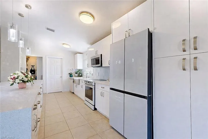 Kitchen featuring hanging light fixtures, white cabinetry, stainless steel appliances, light tile patterned floors, and lofted ceiling