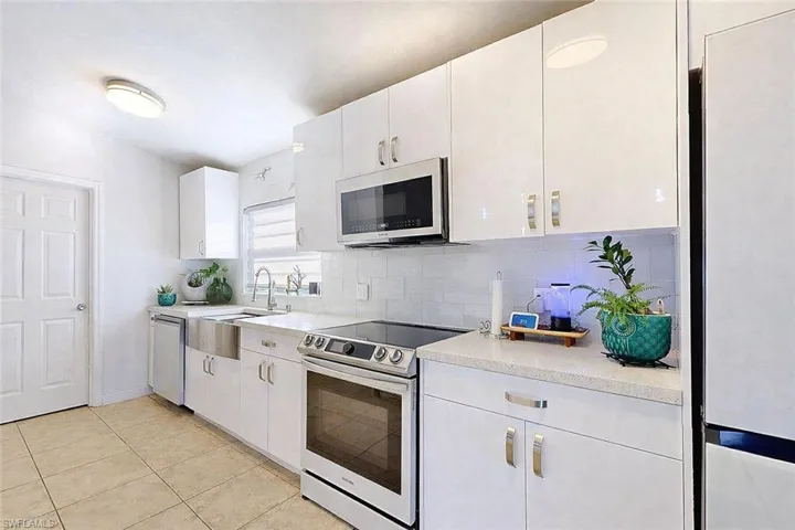 Kitchen with appliances with stainless steel finishes, white cabinets, decorative backsplash, light tile patterned floors, and light stone counters