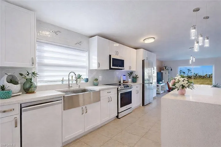 Kitchen with pendant lighting, appliances with stainless steel finishes, white cabinetry, light stone counters, and backsplash