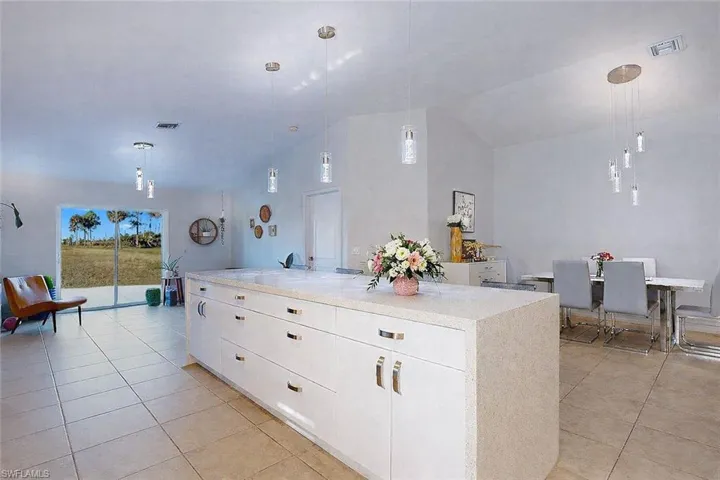 Kitchen with decorative light fixtures, white cabinets, light tile patterned floors, a center island, and light stone countertops