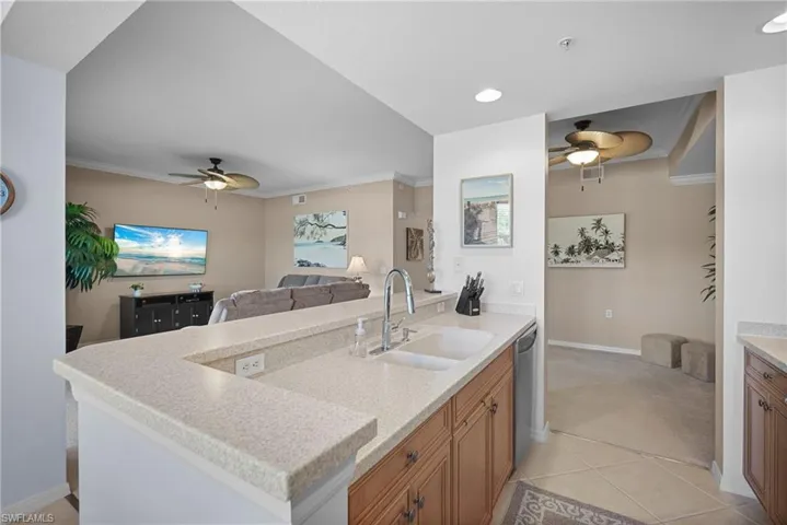 Kitchen with a ceiling fan, brown cabinetry, crown molding, open floor plan, and light tile patterned floors