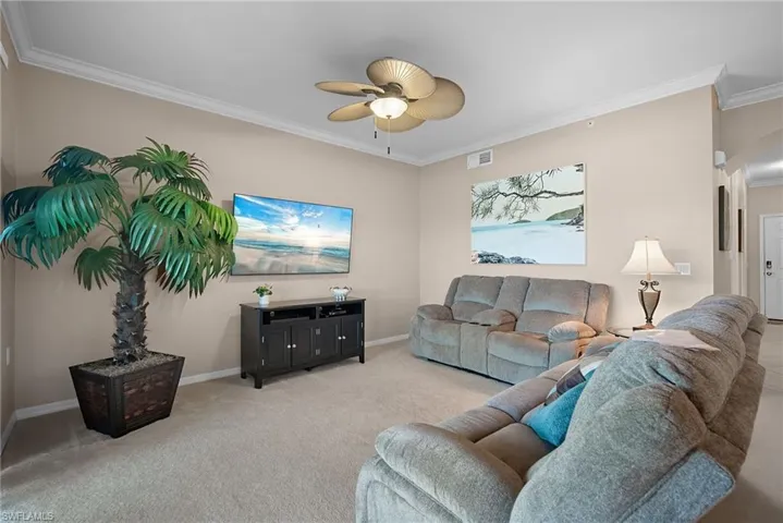 Carpeted living area with crown molding, ceiling fan, and arched walkways