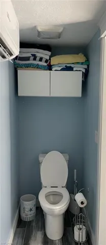 Bathroom featuring a wall mounted air conditioner, wood finished floors, toilet, and baseboards