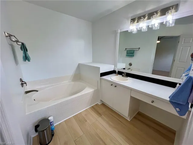 Master Bathroom with  wood-style plank floors, tiled tub, and large vanity