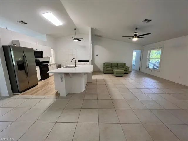 Kitchen with stainless steel fridge, white cabinets, range with electric stovetop, ceiling fan, and vaulted ceiling