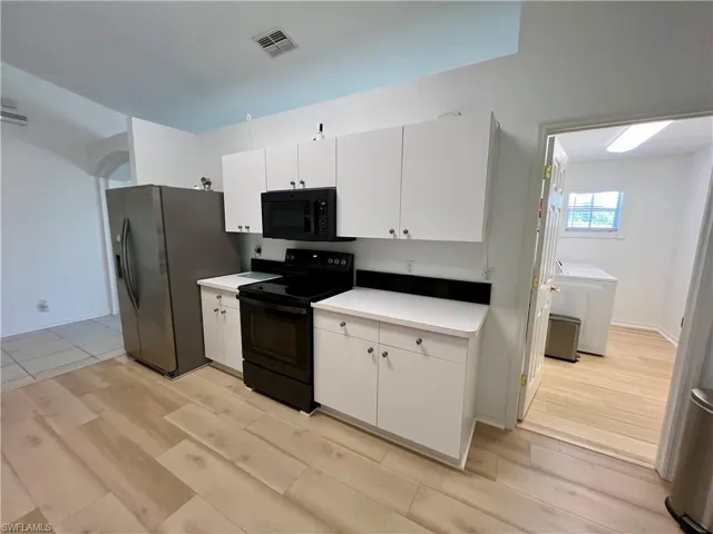 Kitchen with light hardwood / wood-style flooring, white cabinets, and black appliances