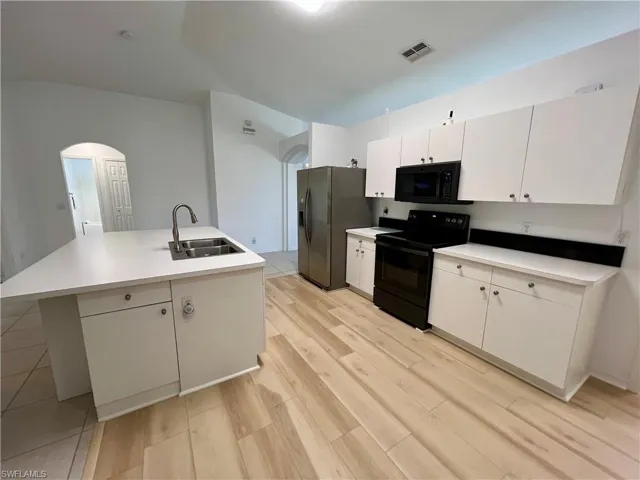 Kitchen featuring light hardwood / wood-style floors, a center island with sink, black appliances, white cabinets, and sink