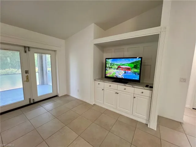 Unfurnished living room with light tile flooring, french doors, and lofted ceiling