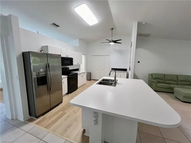 Kitchen featuring light tile flooring, ceiling fan, white cabinetry, black appliances, and sink