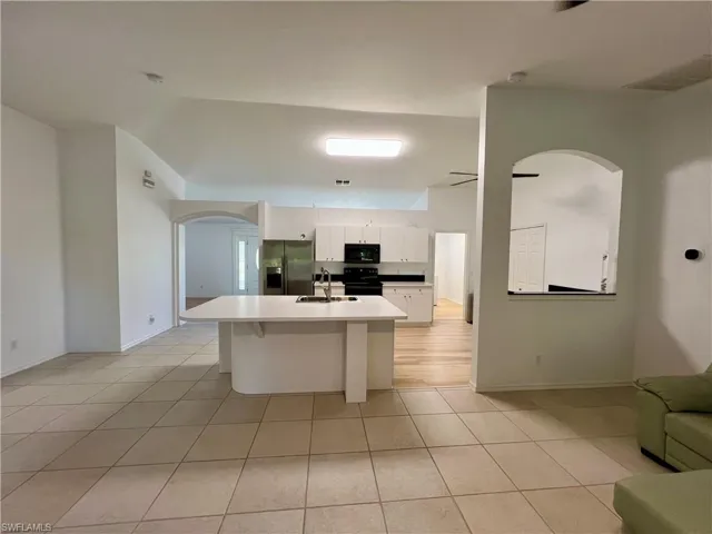 Kitchen with black appliances, light tile floors, sink, white cabinets, and a kitchen island with sink