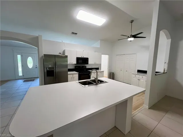 Kitchen with white cabinetry, black appliances, sink, ceiling fan, and light tile floors