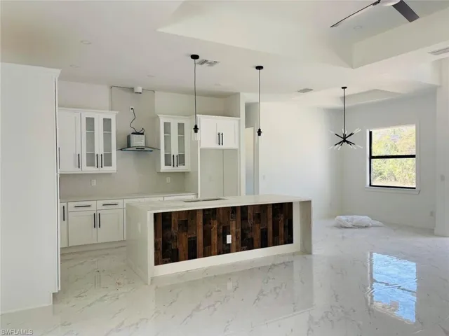 Kitchen featuring a tray ceiling, a kitchen island, marble finish floor, and white cabinetry
