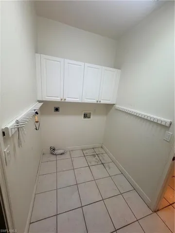 This utility room features white upper cabinetry, tiled flooring, and wall-mounted drying racks