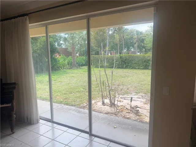Sliding glass doors open to a paved patio and a grassy yard, featuring a hedge and mature trees