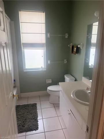 This bathroom features light green walls, a window with blinds, and white tile flooring
