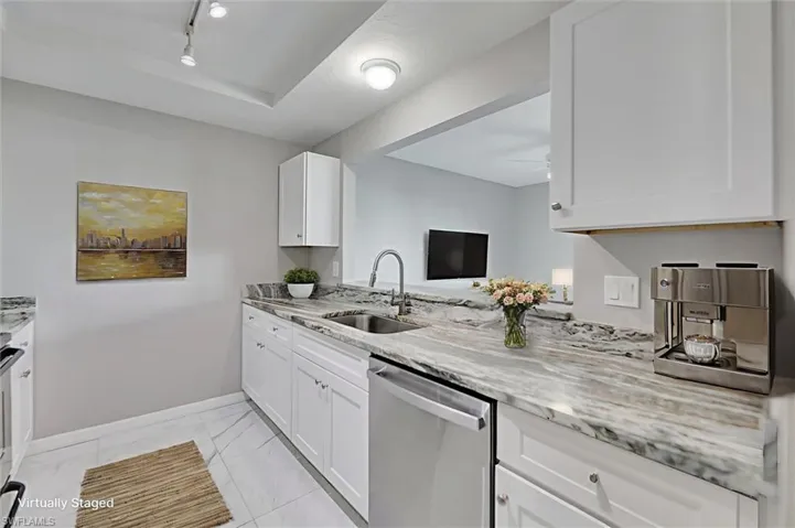 Virtually staged Kitchen featuring dishwasher, white cabinets, light stone countertops, and light marble finish flooring