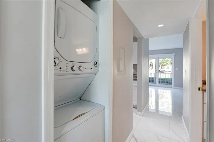 Laundry room with light marble finish flooring, estacked washer and dryer, electric panel, and recessed lighting