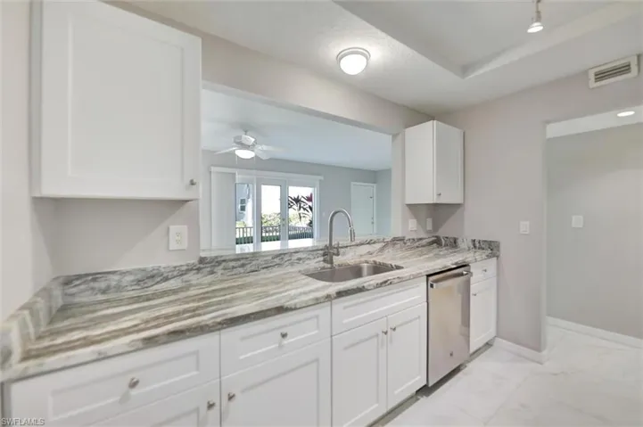 Kitchen with white cabinetry, light marble finish floors, light stone countertops, dishwasher, and ceiling fan