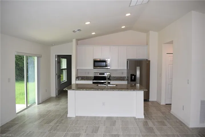 Kitchen featuring a center island with sink, vaulted ceiling, appliances with stainless steel finishes, and light tile patterned floors