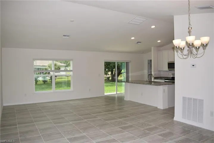 Unfurnished living room featuring sink, light tile patterned floors, vaulted ceiling, and a chandelier