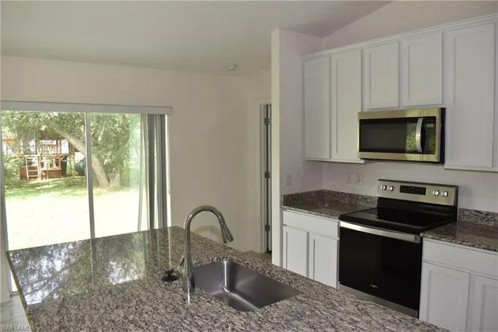 Kitchen with appliances with stainless steel finishes, white cabinets, and dark stone countertops